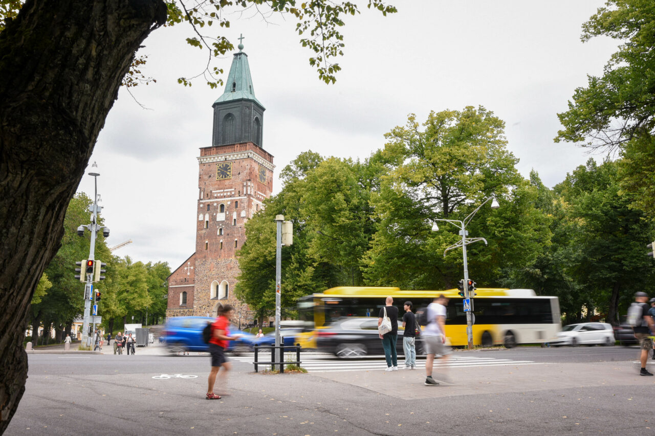 Kuvassa on Turun tuomikirkon edusta, jossa kävelee ihmisiä ja bussi ohittaa kirkon.